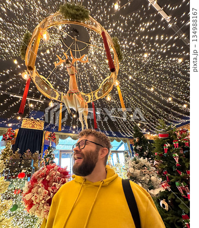 Man smiling under festive Christmas light installation with reindeer decoration. Holiday wonder, christmas magic, joyful exploration, immersive atmosphere, and seasonal delight inside decorated Man smiling under festive Christmas light installation with reindeer decoration. Holiday wonder, christmas magic, joyful exploration, immersive atmosphere, and seasonal delight inside decorated 134988167