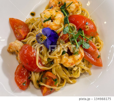 Pasta with shrimp and tomatoes served on white plate close-up. Culinary presentation, gourmet dining, balanced nutrition, seafood cuisine, and sensory enjoyment through refined food preparation. 134988175