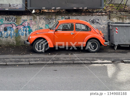 Classic orange vintage car parked along urban street with graffiti wall background. Retro transport style, city character and nostalgic everyday scene 134988188