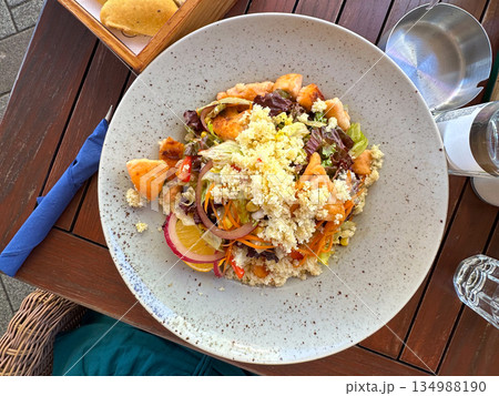 Healthy couscous salad with grilled chicken pieces served on ceramic plate on wooden cafe table. Balanced nutrition, casual dining and mindful eating lifestyle Healthy couscous salad with grilled chicken pieces served on ceramic plate on wooden cafe table. Balanced nutrition, casual dining and mindful eating lifestyle 134988190