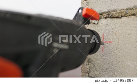 SLOW MOTION,: Builder working uses an electric drill to mount a wall panel. Man drills hole using perforator. Male hands held electric drill with drill bit rotating and making cement dust from wall 134988897