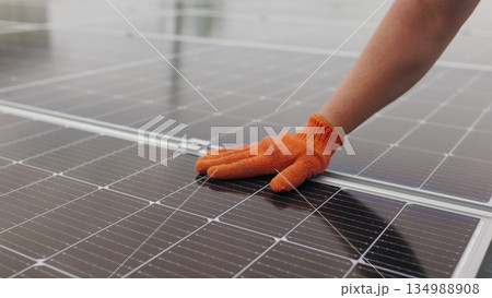 Unrecognizable man glove wiping solar panel from dust on sunny day. Close up of a young engineer hand is checking the operation of sun and cleanliness of photovoltaic solar panels on a sunset Unrecognizable man glove wiping solar panel from dust on sunny day. Close up of a young engineer hand is checking the operation of sun and cleanliness of photovoltaic solar panels on a sunset 134988908