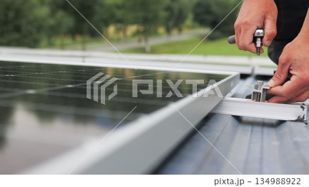 Mounting solar panel, installing solar panels on the roof of the house. Connection of solar panels. Close up of worker installing and working on maintenance of photovoltaic panel system installed Mounting solar panel, installing solar panels on the roof of the house. Connection of solar panels. Close up of worker installing and working on maintenance of photovoltaic panel system installed 134988922