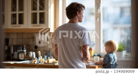 Young father and toddler child spending quiet morning together in bright kitchen by window with natural light 134989009