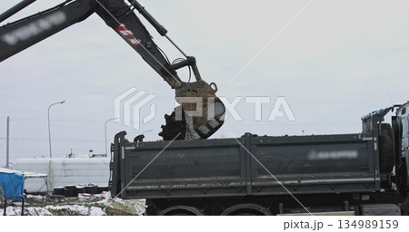 Excavator in action at the construction site. shot: tractor bucket is filling a truck body. A excavator and truck are loading soil. Being prepared for the construction of an industrial facility. 134989159