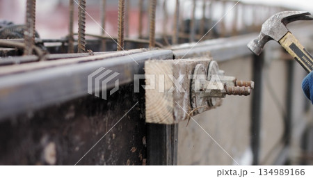 Engineers work with metal constructions while building a house. The worker fixes the form for pouring concrete, aligns metal boards. Filling the foundation of the building. The hammer fixes the form. Engineers work with metal constructions while building a house. The worker fixes the form for pouring concrete, aligns metal boards. Filling the foundation of the building. The hammer fixes the form. 134989166