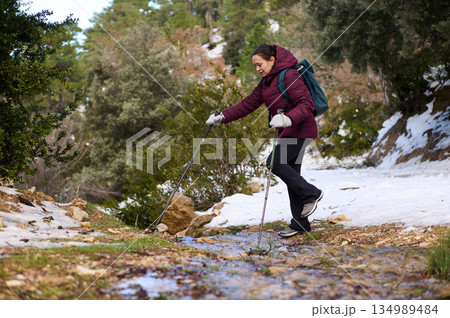 Woman Hiking With Backpack and Poles Through Snowy Forest Trail in Winter Mountain Landscape 134989484