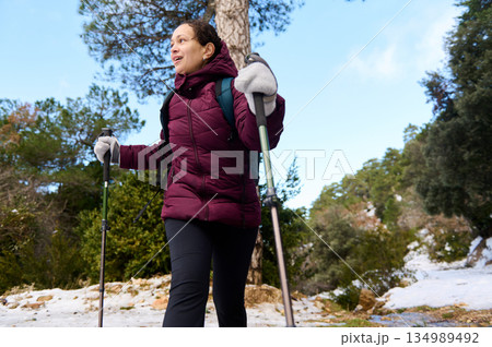 Woman Hiking With Trekking Poles In Snowy Forest On A Cold Winter Day Woman Hiking With Trekking Poles In Snowy Forest On A Cold Winter Day 134989492