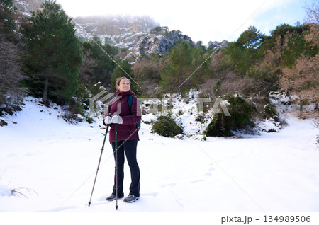 Woman Hiker In Snowy Forest With Trekking Poles On Winter Mountain Trail 134989506