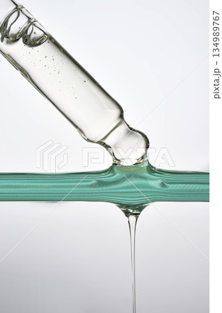 Dropper dispensing clear liquid into green surface Dropper dispensing clear liquid into green surface 134989767