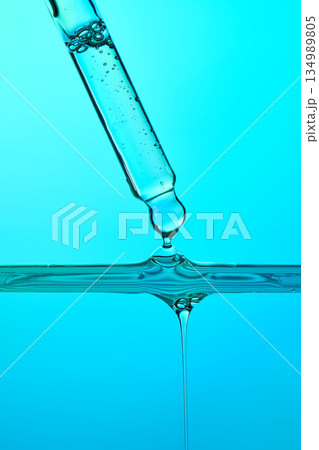 Pipette dispensing clear blue liquid drop into serum Pipette dispensing clear blue liquid drop into serum 134989805