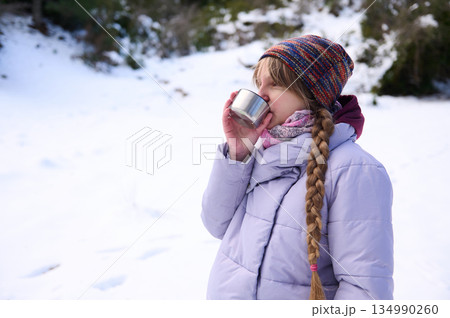 Young Girl In Purple Winter Coat Sips Drink In Snowy Forest On Cold Day 134990260
