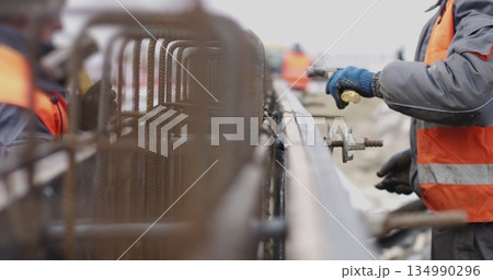 Engineers work with metal constructions while building a house. The worker fixes the form for pouring concrete, aligns metal boards. Filling the foundation of the building. Engineers work with metal constructions while building a house. The worker fixes the form for pouring concrete, aligns metal boards. Filling the foundation of the building. 134990296