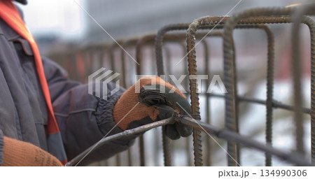 Engineers work with metal constructions while building a house. Close up of worker hands twisting reinforcement to strengthen building foundation. Engineers work with metal constructions while building a house. Close up of worker hands twisting reinforcement to strengthen building foundation. 134990306