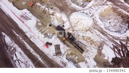 Engineers work with metal constructions while building a house. Aerial Flight Over a New Constructions Development Site. Top Down View at Contractors in Safety Hats Engineers work with metal constructions while building a house. Aerial Flight Over a New Constructions Development Site. Top Down View at Contractors in Safety Hats 134990341