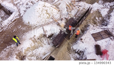Engineers work with metal constructions while building a house. Aerial Flight Over a New Constructions Development Site. Top Down View at Contractors in Safety Hats 134990343