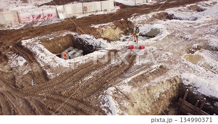 Construction Worker Using Theodolite Surveying Optical Instrument for Measuring Angles in Horizontal and Vertical Planes on Construction Site. Aerial flight over a new construction site. 134990371