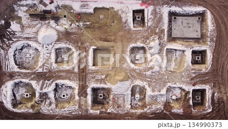 Aerial flight over a new construction site with heavy machinery and people building real estate. Filling the foundation of the building. Top to bottom view of contractors in protective caps. 134990373