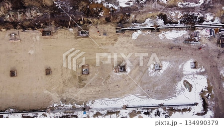 Aerial flight over a new construction site with heavy machinery and people building real estate. Filling the foundation of the building. Top to bottom view of contractors in protective caps. Aerial flight over a new construction site with heavy machinery and people building real estate. Filling the foundation of the building. Top to bottom view of contractors in protective caps. 134990379