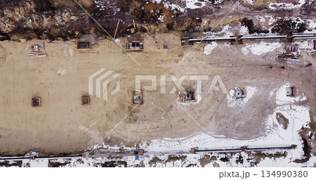 Aerial flight over a new construction site with heavy machinery and people building real estate. Filling the foundation of the building. Top to bottom view of contractors in protective caps. Aerial flight over a new construction site with heavy machinery and people building real estate. Filling the foundation of the building. Top to bottom view of contractors in protective caps. 134990380