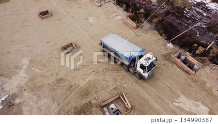 Truck laden with dirt and soil travels in a road construction complex site. Dump truck unloading soil or sand at construction site Truck laden with dirt and soil travels in a road construction complex site. Dump truck unloading soil or sand at construction site 134990387