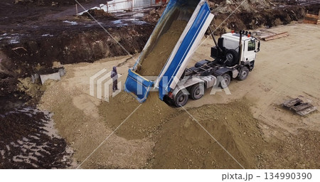 Dump truck unloading soil or sand at construction site. Truck laden with dirt and soil travels in a road construction complex site. Dump truck unloading soil or sand at construction site. Truck laden with dirt and soil travels in a road construction complex site. 134990390
