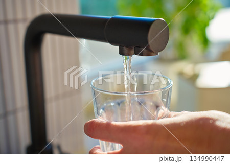 Glass filled with clear water from black kitchen faucet in daylight 134990447