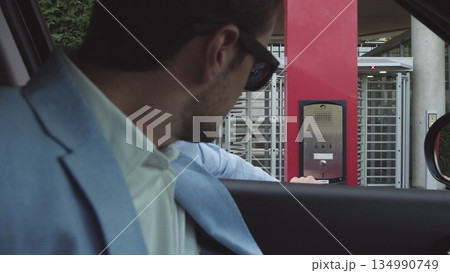 young male businessman in nice suit and glasses paying for parking by bank card with car leaving his office. Office and parking security. 134990749
