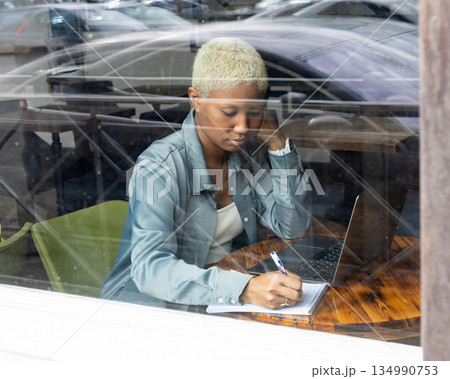 African American woman with short blond hair sits at table and types on laptop. 134990753