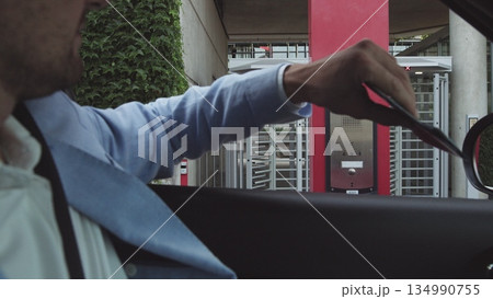 young male businessman in nice suit and glasses paying for parking by bank card with car leaving his office. Office and parking security. young male businessman in nice suit and glasses paying for parking by bank card with car leaving his office. Office and parking security. 134990755