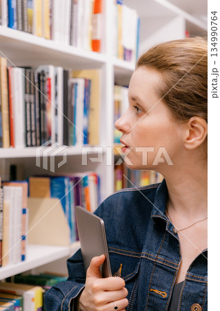 close-up of woman shelves in library, student chooses book. library is filled with books. close-up of woman shelves in library, student chooses book. library is filled with books. 134990764