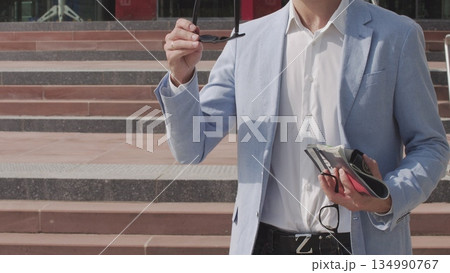 Good-looking confident purposeful adult bearded businessman in glasses in stylish suit going down on steps while leaving the office building and looking at camera. 134990767