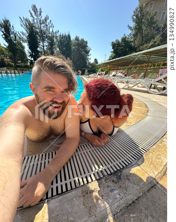 Couple relaxing together at swimming pool edge under sunlight. Summer vacation, shared leisure, intimacy, calm joy and relationship connection during travel 134990827