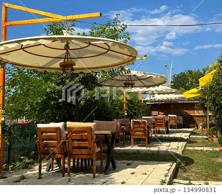 Outdoor cafe garden with wooden tables and umbrellas. Summer dining space, relaxed atmosphere, hospitality and open air leisure Outdoor cafe garden with wooden tables and umbrellas. Summer dining space, relaxed atmosphere, hospitality and open air leisure 134990831