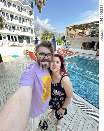 Couple taking selfie near hotel swimming pool outdoors. Vacation mood, travel lifestyle, summer leisure and joyful relationship moment 134990832