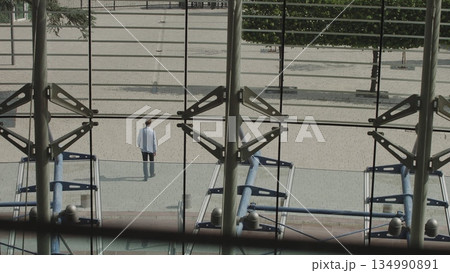 A nicely dressed man leaves a large office, leaves work after a successful working day. Shooting from the building through large glass windows. Panoramic landscape from the office. A nicely dressed man leaves a large office, leaves work after a successful working day. Shooting from the building through large glass windows. Panoramic landscape from the office. 134990891