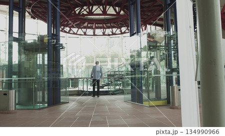 A stylishly dressed man walks down a glass corridor in a modern office. Shooting from the back of the hands. Confident man on his way to work ready to achieve his goals A stylishly dressed man walks down a glass corridor in a modern office. Shooting from the back of the hands. Confident man on his way to work ready to achieve his goals 134990966
