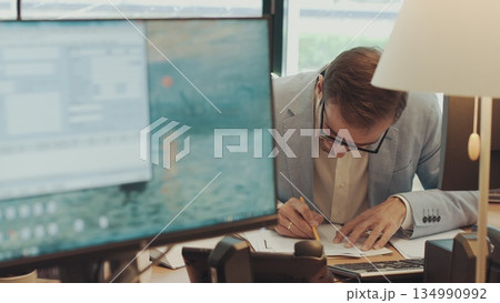 Serious young businessman checking corporate paperwork correspondence sitting at home office desk. Male entrepreneur reading documents, analyzing financial papers, preparing audit report at workplace Serious young businessman checking corporate paperwork correspondence sitting at home office desk. Male entrepreneur reading documents, analyzing financial papers, preparing audit report at workplace 134990992