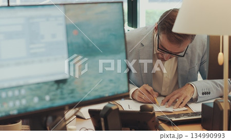 Serious young businessman checking corporate paperwork correspondence sitting at home office desk. Male entrepreneur reading documents, analyzing financial papers, preparing audit report at workplace 134990993