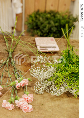 Florist arranging pink carnations and baby's breath on wooden table, mothers day Florist arranging pink carnations and baby's breath on wooden table, mothers day 134991075