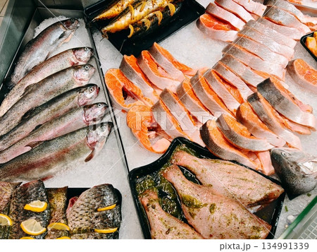 Fresh Fish Counter Display. Whole trout and sliced salmon arranged on crushed ice at supermarket fish counter with various prepared seafood portions. Fresh Fish Counter Display. Whole trout and sliced salmon arranged on crushed ice at supermarket fish counter with various prepared seafood portions. 134991339