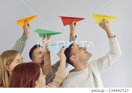 Joyful group of young people enthusiastically launching colorful paper airplanes into air. 134992527