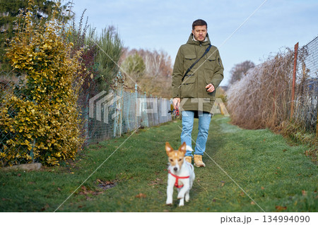 Man walking small dog on leash along green pathway outdoors Man walking small dog on leash along green pathway outdoors 134994090