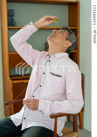 椅子に座って目薬をさす男性 椅子に座って目薬をさす男性 134994211