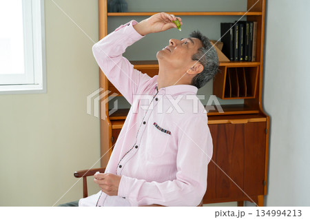 椅子に座って目薬をさす男性 134994213