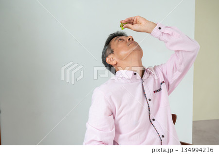 椅子に座って目薬をさす男性 椅子に座って目薬をさす男性 134994216