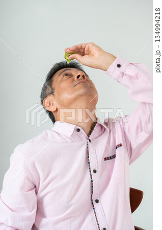 椅子に座って目薬をさす男性 椅子に座って目薬をさす男性 134994218