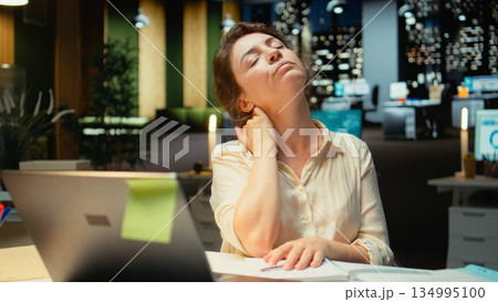 Business employee stretching her upper back and neck muscles, correcting chair posture and neck stiffness for muscle relief and relaxation. Strain due to intense office activity. Camera A. Business employee stretching her upper back and neck muscles, correcting chair posture and neck stiffness for muscle relief and relaxation. Strain due to intense office activity. Camera A. 134995100