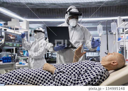 Scientist in protective gear works in biohazard zone to treat a contagious patient, analyzing infection data to advance immunology and epidemic prevention in biotechnology research. Scientist in protective gear works in biohazard zone to treat a contagious patient, analyzing infection data to advance immunology and epidemic prevention in biotechnology research. 134995148