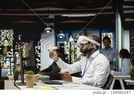 Black businessman using VR headset and gadgets to draft a project plan, engaged in forecasting projections and documenting risk assessment results. Solve tasks with virtual reality. 134995247